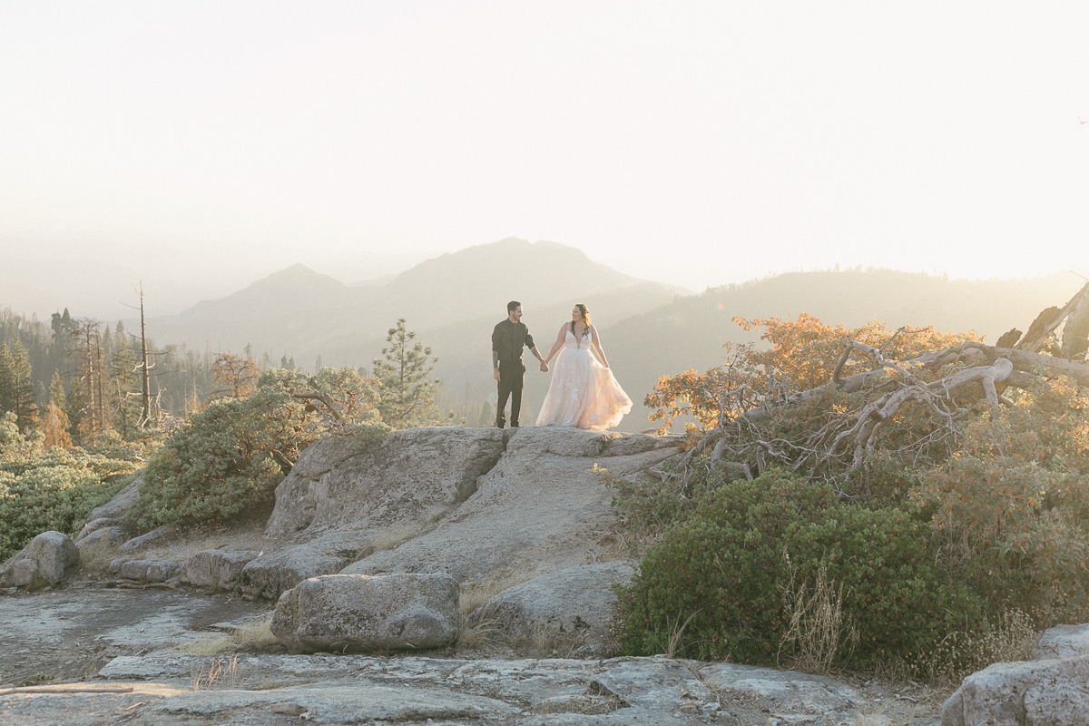 Bride and groom walking on granite at sunset with Sierra foothills in the background